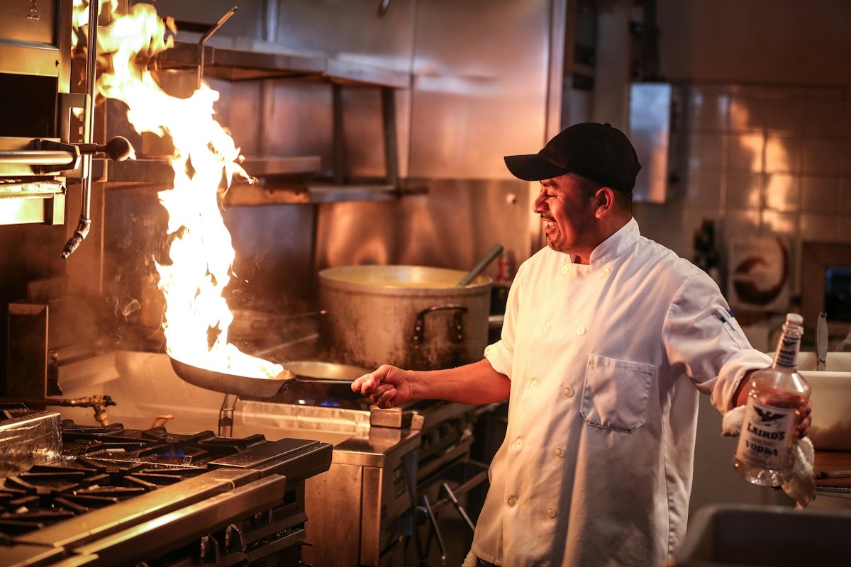 A chef cooking with a flaming pan in a restaurant kitchen